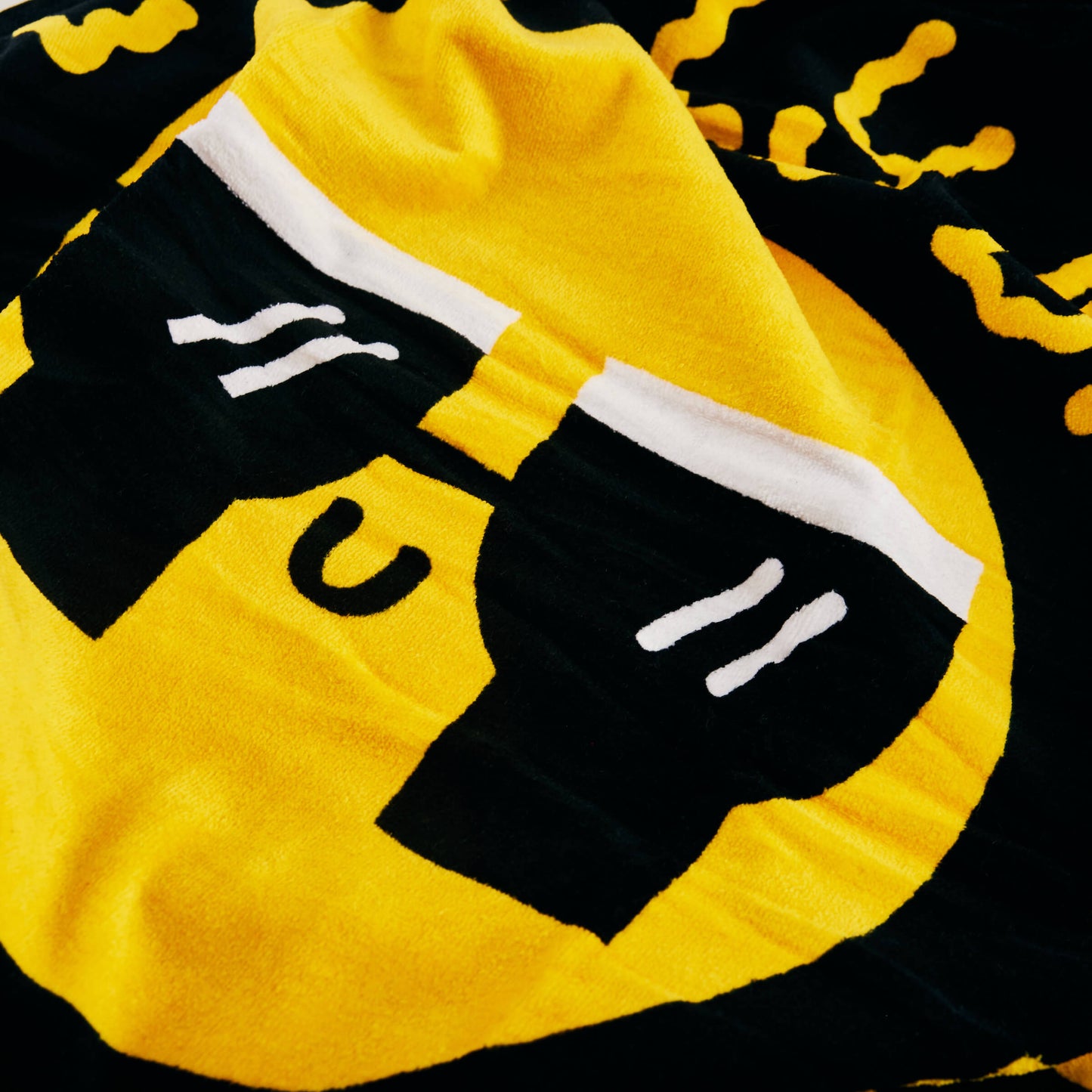 Close-up of the Guinness x Fatti Burke Sun Beach Towel by Guinness, a yellow and black cotton towel featuring a graphic face with sunglasses and a small smile.