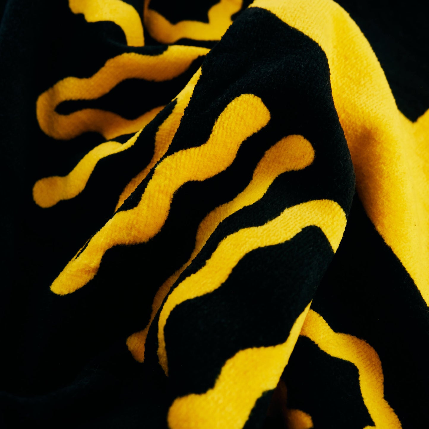Close-up of the Guinness x Fatti Burke Sun Beach Towel by Guinness—black cotton with bold, raised wavy yellow lines in an abstract pattern.