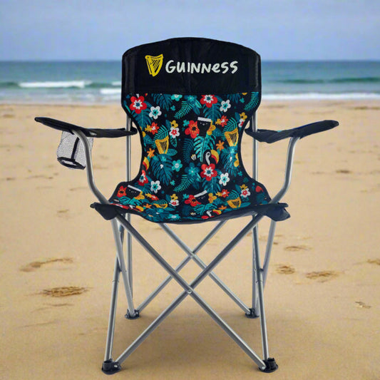 The Guinness x Fatti Burke Hawaiian Camping Chair by Guinness features a floral and logo pattern, armrests, and a mesh cup holder on the left arm, all set against a plain white background.